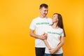 Portrait of young colleagues couple in white t-shirt with written inscription green title volunteer isolated on yellow