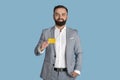 Portrait of young company employee showing credit card on blue studio background