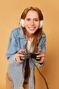 Portrait of young concentrated girl, teenager wearing headphones and playing in video games over ginger background. Game Royalty Free Stock Photo