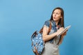 Portrait of young concerned doubtful woman student in grey t-shirt, denim clothes with backpack look aside writing on