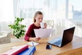 Portrait of young confident business woman sitting at wood desk, drinking coffee and reading documents at home office Royalty Free Stock Photo