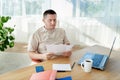 Portrait of young confident businessman sitting at wooden desk and working with documents and laptop in modern office, copy space Royalty Free Stock Photo