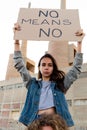 Portrait of young confident woman hold no means no banner in woman empowerment demonstration . Sitting on mans shoulder.