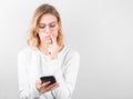 Portrait of a young confused girl in white short holding mobile phone isolated over white background