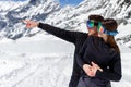 Portrait of a young couple embrace, wear in goggles, man showing by arm a point a side, mountain landscape background. Royalty Free Stock Photo