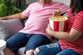 Portrait of young couple laughing, eating popcorn, sitting on the sofa watching TV at home Royalty Free Stock Photo