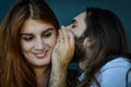 Portrait of a young couple where bearded man with long hair tells a funny secret to the woman with red hair and she smiles Royalty Free Stock Photo