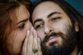 Portrait of a young couple where a red-haired woman tells a secret to the man bearded her ear covering her mouth