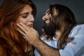 Portrait of a young couple where the young man with beard and long hair caresses the face of the young woman with long red hair Royalty Free Stock Photo