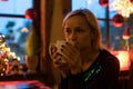 Portrait of a young cozy with cup of coffee, cookie and Christmas lights and pine branch. Royalty Free Stock Photo