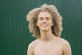 Portrait of a young curly-haired guy on the street against a green fence. topless young man