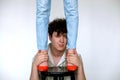 Portrait of young curly handsome man sitting at black stool holding feet of unrecognizable woman standing on stool.