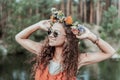 Portrait of young curly woman with floral chaplet enjoying weekend in forest