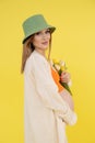 Portrait of young cute barefoot pregnant woman wearing green bucket hat, orange top, standing, holding bunch of tulips. Royalty Free Stock Photo