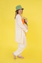 Portrait of young cute barefoot pregnant woman wearing green bucket hat, orange top, standing, holding bunch of tulips. Royalty Free Stock Photo