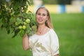 Portrait of a young cute blonde white girl near the tree with green apples. Royalty Free Stock Photo