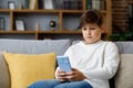 Portrait of young cute boy holding smartphone sitting at sofa. Teenager at home choosing favorite music, texting