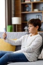 Portrait of young cute boy holding smartphone sitting at sofa. Teenager at home choosing favorite music, texting