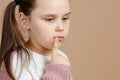 Portrait of young cute sad pensive blue-eyed girl with long dark hair in white and pink sweater standing with index