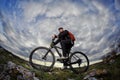 Portrait of the young cyclist standing with bike on the rocks against dramatic sky with clouds. Royalty Free Stock Photo