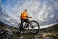 Portrait of the young cyclist standing with bike on the rocks against dramatic sky with clouds. Royalty Free Stock Photo