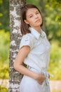 Portrait of young dark-haired woman embracing birch tree