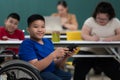 Portrait of young disabled boy with firmly eyes sitting on wheelchair in classroom and holding table computer in hand Royalty Free Stock Photo