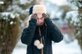 Portrait of a young discontented Caucasian woman in a hat with earflaps and a jacket that scratches her forehead. Winter season, Royalty Free Stock Photo