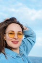 Portrait of young diverse woman in yellow glasses smiling, standing by seaside