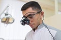 Portrait of Young doctor with dental binocular loupes on his face at dentist clinic.