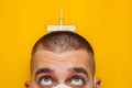 Portrait of a young doctor in a respirator on a yellow background. An ampule with a coronavirus vaccine on the head. Look into the