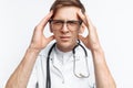 Portrait of a young doctor, on a white background, which depicts a headache, trainee in the Studio, with a stethoscope on the neck Royalty Free Stock Photo