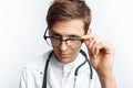 Portrait of a young doctor, on a white background, who takes off his glasses and looks at the camera, a trainee in the Studio, wit Royalty Free Stock Photo