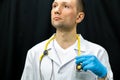 Portrait of a young doctor in a white coat on a black background. A doctor in blue gloves and with a medical stethoscope around Royalty Free Stock Photo