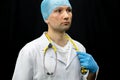 Portrait of a young doctor in a white coat on a black background. A doctor in blue gloves and with a medical stethoscope around Royalty Free Stock Photo