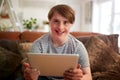 Portrait Of Young Downs Syndrome Man Sitting On Sofa Using Digital Tablet At Home Royalty Free Stock Photo