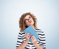 Portrait of a young dreaming girl with glasses holding an old book in her hands and looking up thoughtfully, on light blue Royalty Free Stock Photo