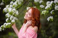 Portrait of young dreaming woman in romantic pink dress in a blooming apple garden.