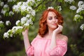 Portrait of young dreaming woman in romantic pink dress in a blooming apple garden.