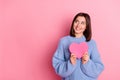 Portrait of young dreamy smiling woman holding pink paper heart want peace looking empty space isolated on pink color Royalty Free Stock Photo