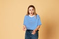 Portrait of young, emotive blonde girl in striped shirt standing with misunderstanding face against yellow studio Royalty Free Stock Photo