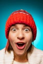 Cropped portrait of young, excited merry girl in red winter hat posing at camera isolated over blue background Royalty Free Stock Photo