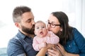 Portrait of young family with baby daughter sitting indoors on a sofa, kissing her. Royalty Free Stock Photo