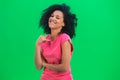 Portrait of young female African American flirtatious smiling. Black woman with curly hair in pink tshirt poses on green