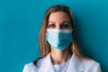 Portrait of young female doctor in medical mask and white gown on blue background. Royalty Free Stock Photo