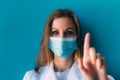 Portrait of young female doctor in medical mask and white gown on blue background. Royalty Free Stock Photo