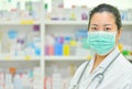 Portrait of young female doctor wear mask on many medicine shelf background.