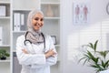 Portrait of young female doctor wearing hijab, Muslim woman smiling and looking at camera with arms crossed in white Royalty Free Stock Photo