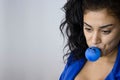 Portrait of young female executive dressed in blue and holding a blue balloon in her mouth with a sad face drawn on the blue