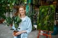 Portrait of young female florist holding ficus flowerpot looking at camera